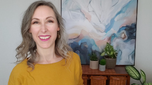 Erin Acton smiles with abstract painting and potted plants behind her