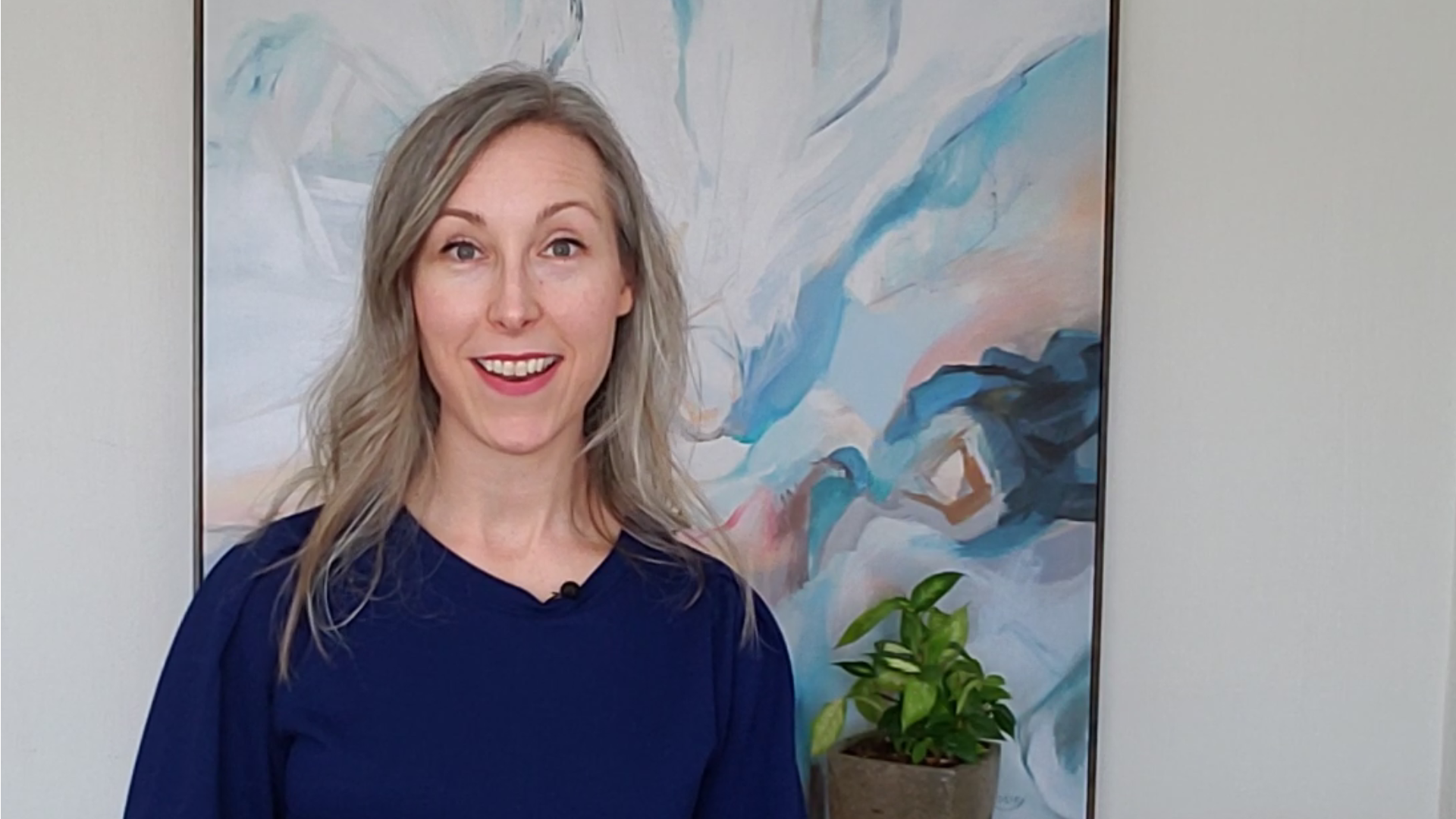 Erin Acton smiles mid-speech. Abstract painting and plants are on wall behind her.